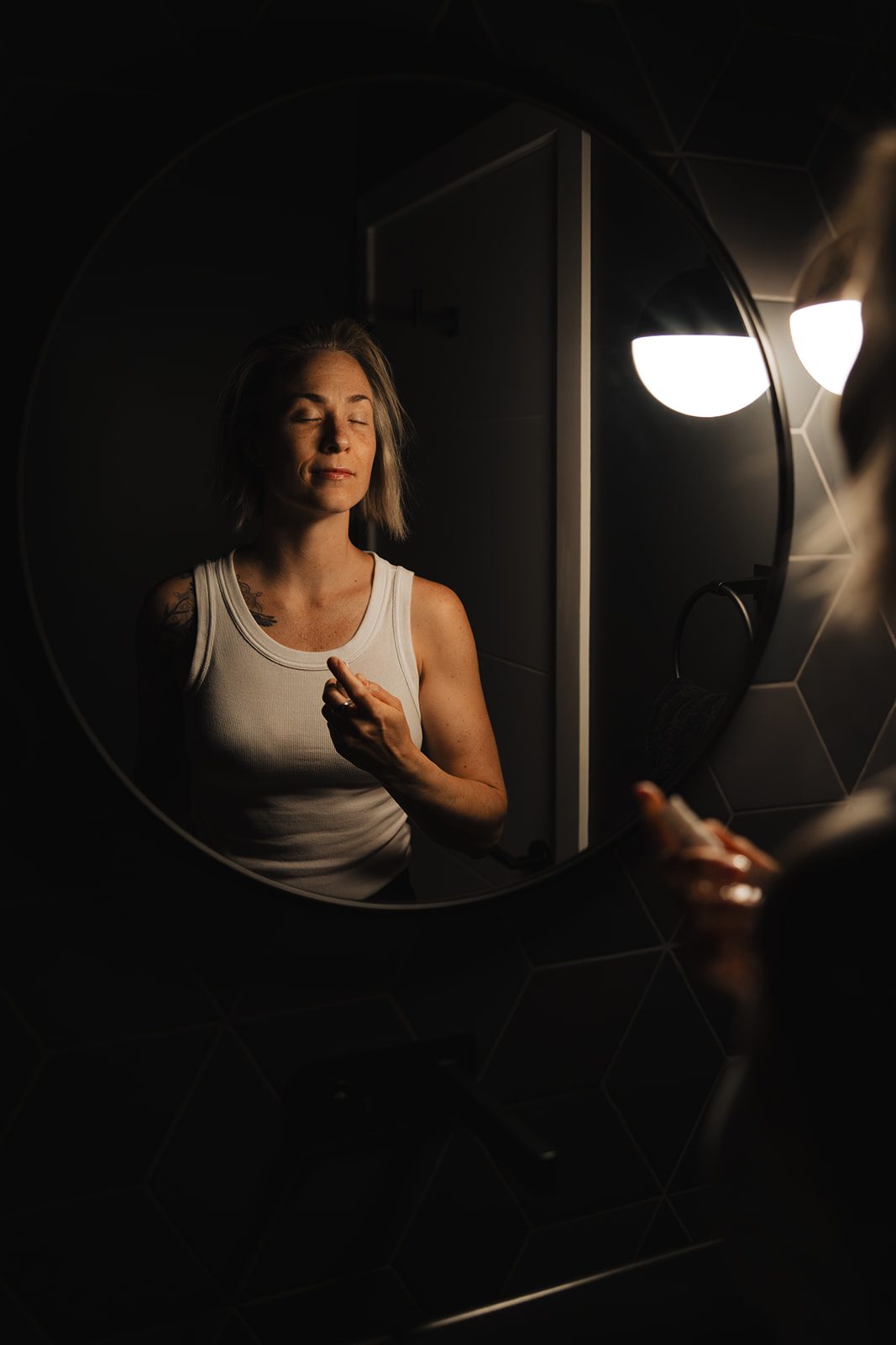Person stands in front of mirror with skincare product in hand.