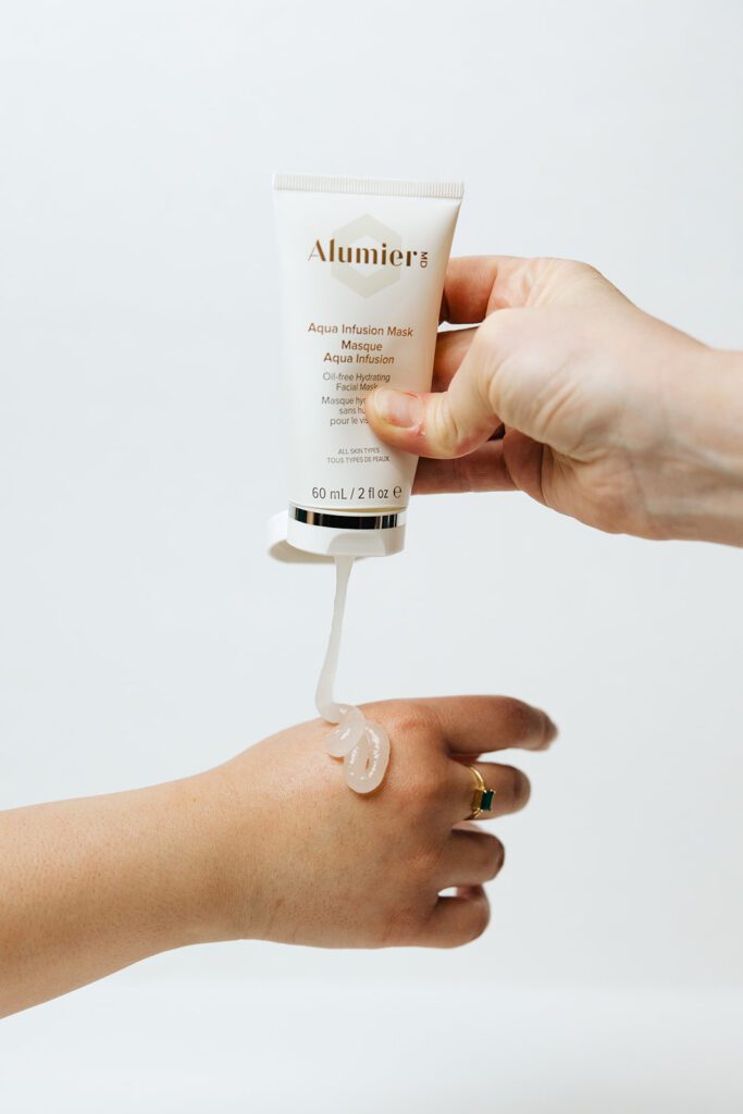 ONYX Beauty Lab | The Onyx Beauty Lab 2025 Holiday Gift Guide Alumier Aqua Infusion Mask bottle is squeezed and pours out onto a hand.